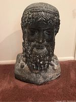 Front view of heavy stone bust sculpture depicting Poseidon. Shows detailed facial features with curly hair and beard.