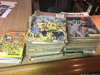 Two stacks of vintage Boys Life magazines under natural light on wooden table including a yellow scouting magazine on left