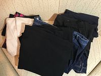 Photo showing a pile of women's pants and skirts in mostly black, navy, and beige colors, with some denim jeans.