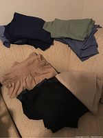 Seven pairs of women’s pants in various colors with elastic waistbands, folded and laid out on a beige surface.