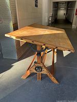 Angled side view of the drafting table showing the wooden top, iron adjusting handles, and supporting wooden base.