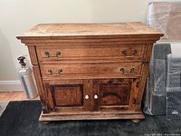 Front view of antique dry sink cabinet showing two metal-handled drawers and two wooden doors with white knobs, wooden textured surface with rustic refinishing.
