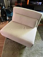 Photo of modern folding chaise lounge chair in creamy white fabric, showing seat, backrest, and lumbar pillow, placed on a patterned carpet with visible surroundings.