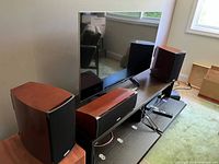 Three Polk Audio speakers with walnut finish and black grille, arranged on a TV stand without the TV screen.