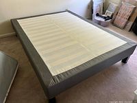 Top-down angled view of the Ikea queen bed frame showing the grey fabric base and white slatted support surface.