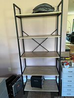 Metal frame bookcase with wood veneer shelves, empty except for a bag on the top shelf and items on the floor beneath it.