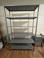 Front view of assembled Ikea metal utility shelving unit showing six flat metal shelves and gray metal frame.