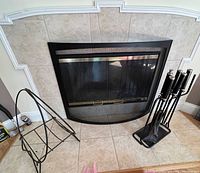 Front view of modern fireplace with black and gold fire screen, metal log holder, and fireplace tools set