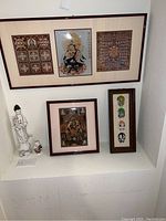Overall view showing framed artworks and porcelain figurines arranged on white ledge and wall.