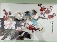 Full framed shell art showing two birds on a branch with colorful flowers and leaves inside a white shadow box frame.