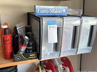 Photo showing assortment of car care bottles including orange, red Klasse bottle, black spray bottles, and Euro-Shine box on shelf.