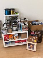 Wide view of white shelving unit with coffee and tea appliances, containers, and boxed pods