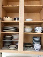 Open kitchen cupboard showing stacks of plates, bowls, and containers on three shelves.