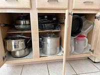 Open kitchen cupboards showing various pots, pans, and plastic storage containers neatly arranged on shelves.