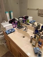 Bathroom sink and counter with assorted toiletries including lotions, mouthwash, soaps, hairbrushes, combs, and personal care items around mirror and faucet