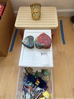 Plastic storage bin with white lid, two heart-shaped floral boxes on top, and a golden green glass on a beige surface