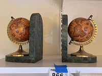 Side view of two globe bookends with brown-tone globes on brass bases and dark green marble stands.