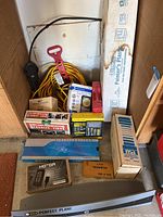 Contents under workbench showing various boxed electrical items, cords, and measuring tools arranged on shelf.