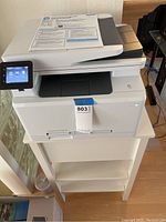 Overall front view showing the printer and the stand it sits on, with a document on top of the printer.