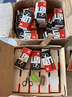 View inside open boxes filled with individual boxes containing miniature folding scissors, some loose scissors displayed on top.