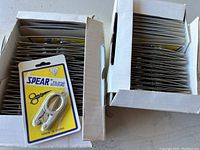 Two boxes filled with individually packaged small folding scissors labeled Spear Folding Scissors, made in China.