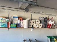 Shelf holding all paper products and cleaning supplies, visible wall hooks and hooks below.