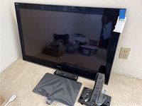 Sony KDL-40NX700 40-inch BRAVIA LCD TV leaning against wall with remote and TV stand parts on floor in front.