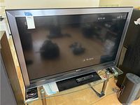 Sony 52 inch LCD TV powered off on stand with remote on top shelf with visible reflections in screen