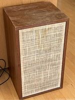 Overall front view of the wooden speaker cabinet with fabric grille covering the front.