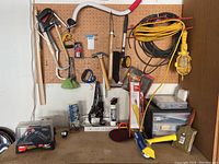 View of pegboard and workbench with hanging hand tools including saw, hammer, pliers, scissors, and extension cords.
