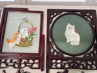 Two wood framed embroidery pieces depicting cat designs on silk fabric, front view showing the detailed craftsmanship and carved frames.