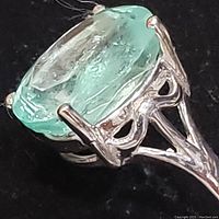 Close-up of oval green emerald in gold prong setting from angled side