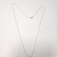 Full view of the 18 inch thin yellow gold necklace on a white background, laid flat showing entire chain and clasp.