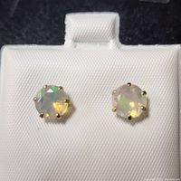 Close-up photo of round faceted natural opal stud earrings in 10K yellow gold setting showing the play of colors and prong setting.
