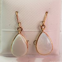 Front view of both teardrop opal earrings hanging side by side on a white textured pad