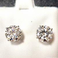 Front view of both earrings on white textured background showing round cut stones and four-prong settings