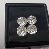 Four round brilliant cut white moissanite stones in a black display box viewed from above