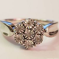 Close-up front view of silver ring with 7 small diamonds in a floral cluster setting.