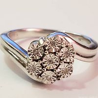 Close-up front view of silver ring with 7 round cubic zirconia stones in cluster setting