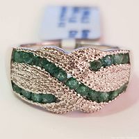 Front view of silver ring with textured design and green emerald stones inlaid in three rows.