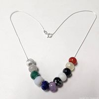 Silver necklace laid flat showing 11 gemstone beads arranged in a row at the center with the clasp visible