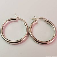 Overhead photo showing pair of silver hoop earrings lying flat with hinged snap closure visible.