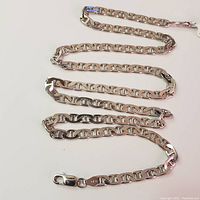 Silver necklace chain laid out on white surface, showing full length and overlapping links.