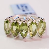 Close-up front view of silver ring with five marquise-cut peridot stones.
