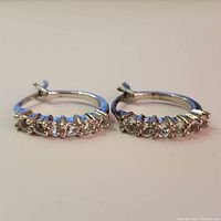 Pair of silver hoop earrings set with clear white topaz stones shown side by side on white surface.
