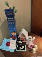 Photo showing assorted Halloween and Christmas decorative items including Charlie Brown Christmas tree in box, ceramic gingerbread house, angel and airplane ornaments, mini purple spider string lights, two wind-up walking ghosts, red ornament, and drawing.