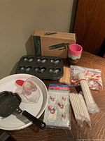 Photo of baking lot showing heart-shaped pan, Stormtrooper pancake mold, white Corningware plate, IKEA baking cups, candy/cakepop sticks, snowman bags, and Pampered Chef decorator set in box.