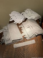 Grey and white folded curtain panels and matching grey tie-backs on wooden surface, showcasing fabric texture, tab tops and color.