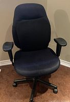 Front view of navy blue desk chair showing padded seat, backrest cushion, armrests, and caster base