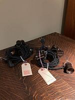 Two bundles of black vintage reproduction fabric cord indoor light strings each with multiple lamp sockets and attached tags.